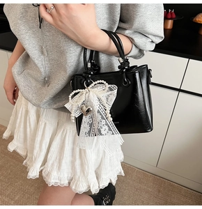 Détail d'un sac seau noir brillant avec grand nœud en dentelle blanche et perles