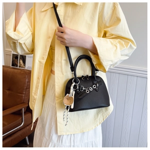 Detailed view of black litchi pattern shell bag with a baseball charm and shoulder strap