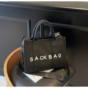 Close-up of black canvas sack bag with wide nylon strap on a vintage leather chair