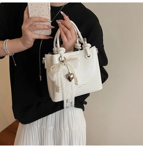 Détail d'un sac seau blanc avec breloque cœur en dentelle perlée et poignée nouée