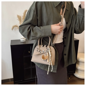 Detail of beige shell-shaped crossbody bag with lychee texture and heart charm pendant
