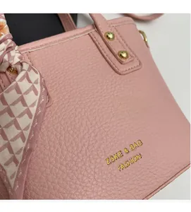 Detail of pink lychee leather handbag featuring gold studs and houndstooth silk scarf handle