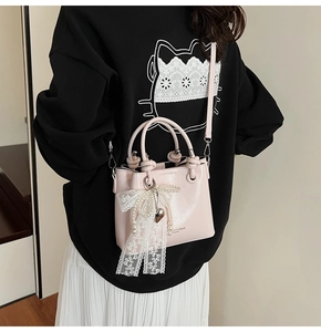 Détail du sac bandoulière rose clair avec nœud en dentelle blanche et perles élégantes
