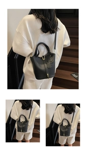 Detail of black pebbled leather bucket bag with gold lock and smiling face charm