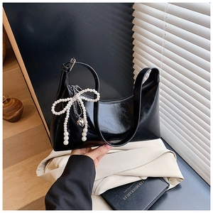 Détail du sac à bandoulière en cuir noir brillant avec nœud perlé et pendentif cœur