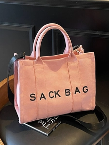 Pink canvas tote bag with black strap and SACK BAG print shown on a leather chair