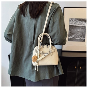 Detail of beige shell-shaped bag with litchi texture, metal chain, and cute bear pendant