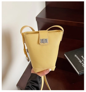 Détail d'un sac seau en cuir grainé jaune vif avec fermoir rotatif argenté et lanière