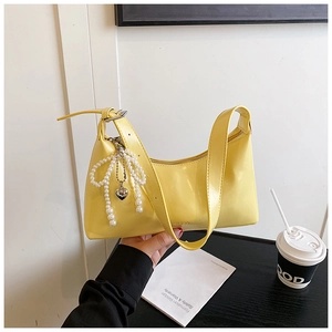 Détail du sac hobo en cuir souple jaune vif avec nœud en perles et pendentif coeur argenté