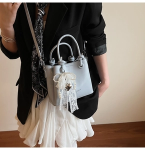 Détail du sac seau en cuir bleu clair avec nœud en dentelle perlée et décor de cœur