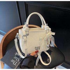 Detailed shot of white lychee leather bucket bag with pearl lace bow and metal heart charm