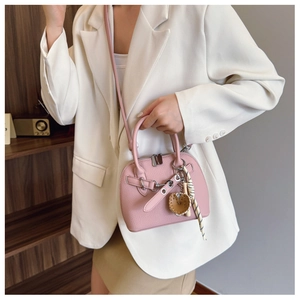 Pink lychee texture shell bag shown with heart charm and striped ribbon on white blazer