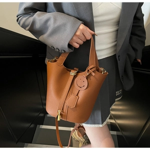 Detail of brown litchi pattern leather bucket bag with gold lock and smiley face pendant