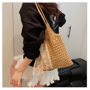 Detailed view of woven straw shoulder bag featuring white lace and pink rose embroidery