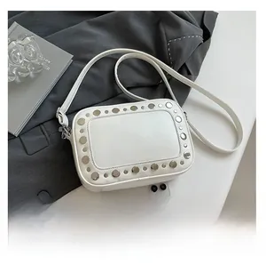 Detailweergave van witte lederen crossbody cameratas met zilveren klinknagels op een pak