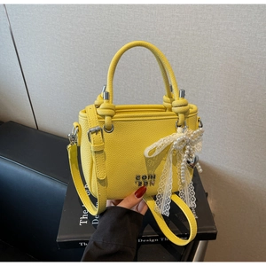 Detail of yellow lychee leather bag with knot handle and pearl lace bow charm