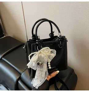 Détail d'un sac seau noir avec nœud en dentelle blanche, perles et pendentif cœur argenté