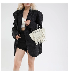 Dettaglio borsa bianca con frange e borchie argentate su un blazer nero da passerella