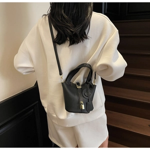 Rear view of model wearing black lychee leather bucket bag with gold H clasp hardware