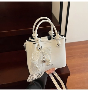 Détail du sac seau en cuir blanc avec nœud en dentelle de perles et breloque cœur