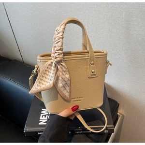 Detail of beige lychee textured bucket bag featuring a silk scarf on the handle