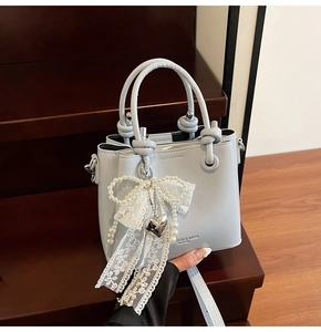Gros plan du sac seau en cuir bleu clair avec nœud en dentelle et breloque perle