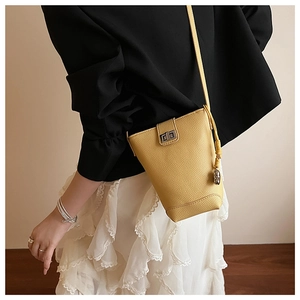 Détail du sac seau jaune en cuir grainé avec fermoir en métal doré et pompon chic