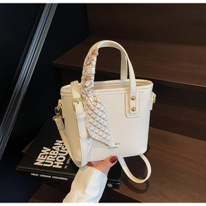 Close-up of beige lychee texture bucket bag with decorative silk scarf and gold logo