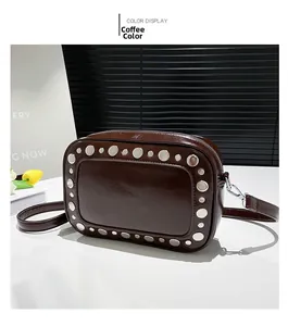 Detail van bruine glanzende leren crossbodytas versierd met zilveren metalen studs