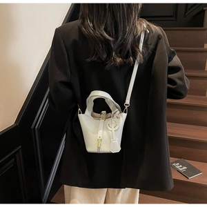 Detail view of a white leather bucket bag with a golden lock and a smiley face charm