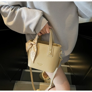 Macro view of beige lychee texture leather handbag with gold logo and silk scarf detail