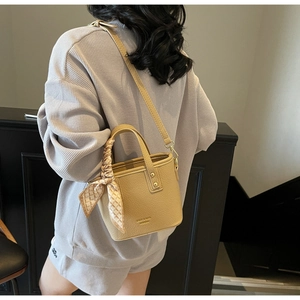 Detail of khaki litchi textured bucket bag with decorative silk scarf on handle