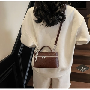 Detail view of brown ostrich pattern leather bag with silver zippers and key pendant