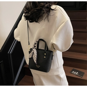 Detail of black litchi grain leather bucket bag with silk scarf handle and golden hardware