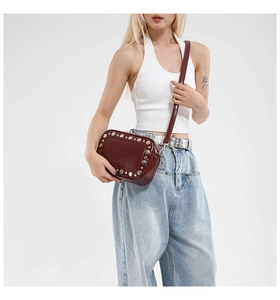 Detail van bordeaux crossbodytas met zilveren klinknagels gedragen op jeans en top