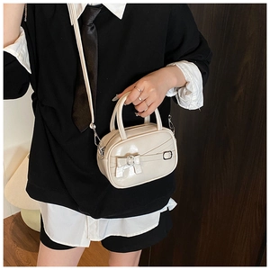 Chic cream bowling bag with leather bow and metallic buckle shown in a lifestyle shot