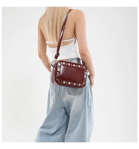 Dettaglio di una borsa fotografica rosso scuro con borchie argentate su sfondo bianco