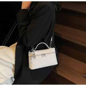 Detailed close-up of a white ostrich-embossed handbag featuring a metal lock and key charm