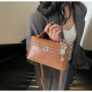 Detail of ostrich embossed brown handbag featuring silver dual zippers and logo pendant