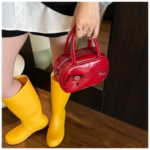 Detail view of a red patent leather bowling bag featuring a metallic bow and zipper closure
