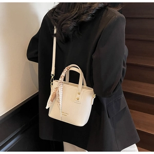 Beige lychee pattern bucket bag with silk scarf on handle worn by model on stairs