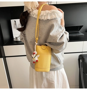 Vue de dos d'un mannequin portant un sac bandoulière jaune motif litchi avec breloque canard