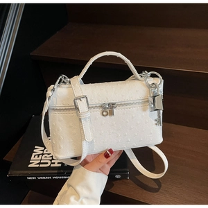 Detail of white ostrich texture handbag with silver lock charm on dark wood background