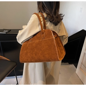 Detalle de un bolso tote grande de ante marrón llevado por una modelo en un ambiente cálido
