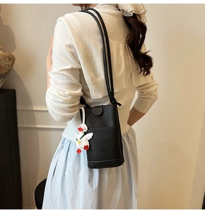 Détail d'un sac seau noir grainé avec un charmant pendentif en peluche de canard blanc