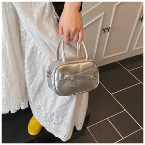 Close-up of metallic silver bowling handbag with bow detail held by a model in white dress