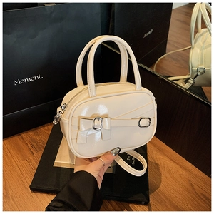 Macro detail of creamy glossy leather bowling bag with metallic bow buckle and crossbody strap