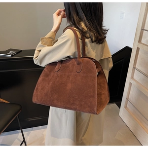 Detalle de un bolso grande de ante marrón llevado por una modelo con una gabardina beige