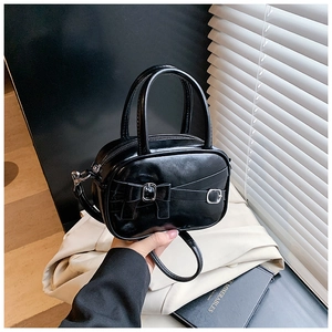 Detail of a glossy black mini bowling bag with leather bow and metallic buckle