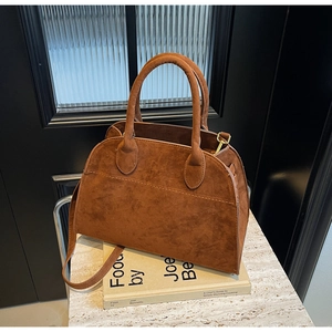 Detalle del bolso Boston de ante marrón con correa en una superficie de piedra mínima